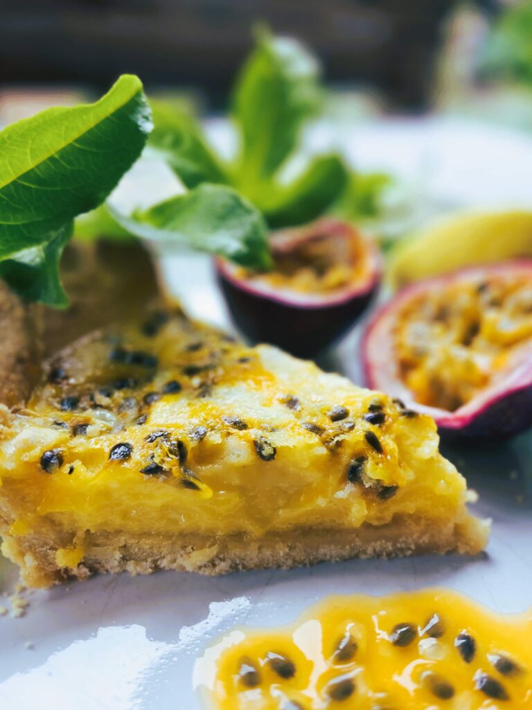 Slice of Passionfruit Lemon Tart with drizzle of passionfruit juice and fresh halved passionfruit